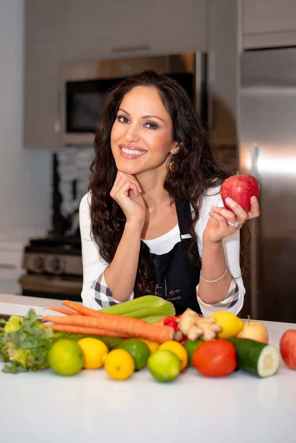Cheryl Martinez with fresh produce, holding a red apple in her kitchen